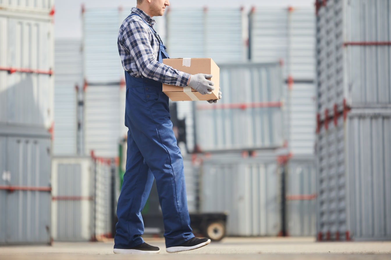 A person in blue overalls carrying a box.